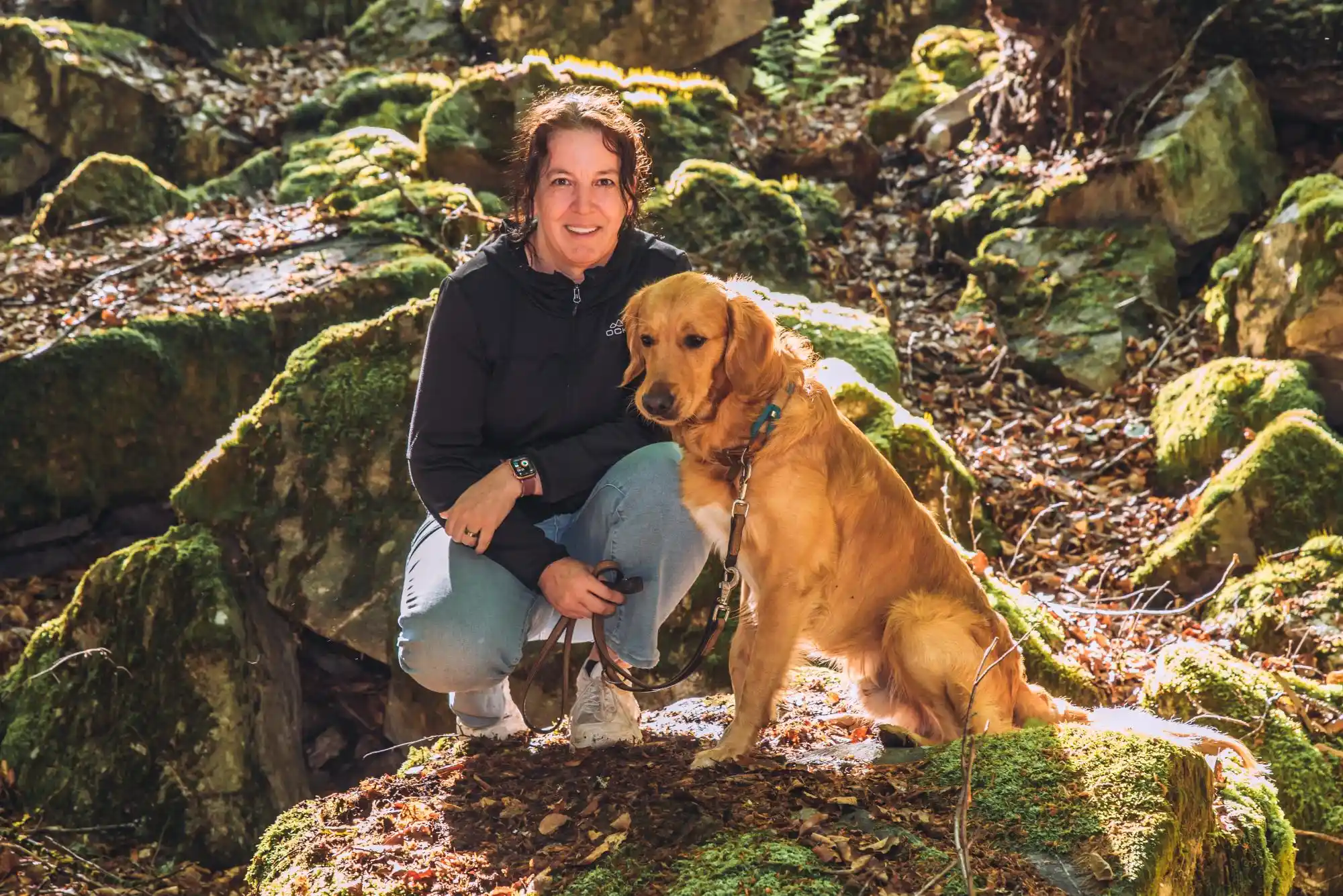 Kerstin Ehses lächelt zur Kamera; neben ihr sitzt ein Golden Retriever mit geschlossenem Maul.